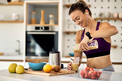 mujer con ropa de ejercicio preparando un batido de proteína bimanan