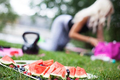 frutas en un plato sobre el césped verde y mujer al fondo haciendo una rutina de ejercicio